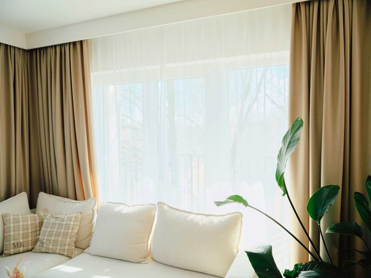 Wohnzimmer mit stilvollen Vorhängen Gemütliches Wohnzimmer mit beigen Vorhängen und grüner Pflanze